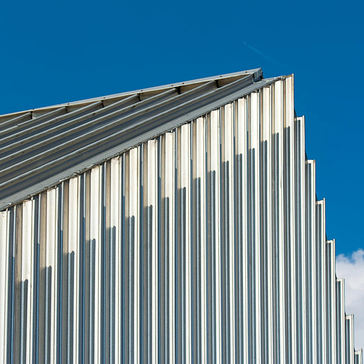 Architectural lines on a corrugated industrial building against a clear blue sky